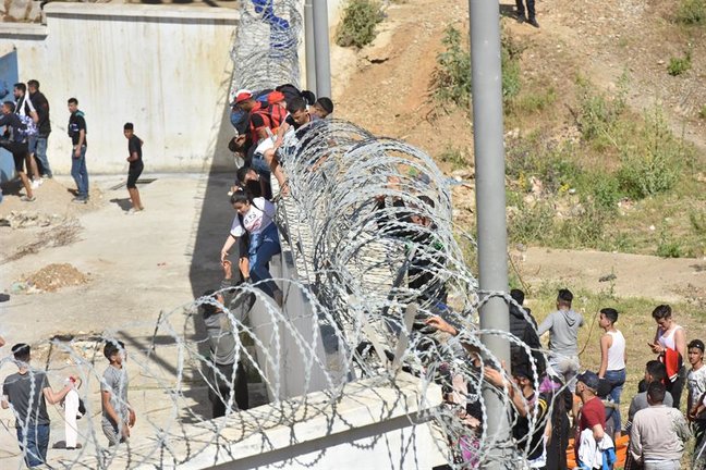 Migrantes escalan la valla en la ciudad norteña de Fnideq en un intento de cruzar la frontera de Marruecos al enclave español de Ceuta. / EFE