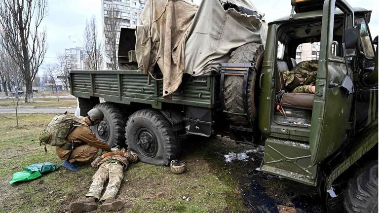 Un médico militar ucraniano examina el cuerpo de un soldado ruso vestido con un uniforme militar de Ucrania, junto a un camión militar, tras una escaramuza en Kiev. Dentro del vehículo yace otro cuerpo. AFP / SERGEI SUPINSKY
