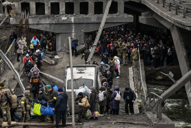 Un grupo de personas cruza un puente destruido mientras evacua la ciudad de Irpin, al noroeste de Kiev, durante un intenso bombardeo el 5 de marzo de 2022. ARIS MESSINIS/AFP