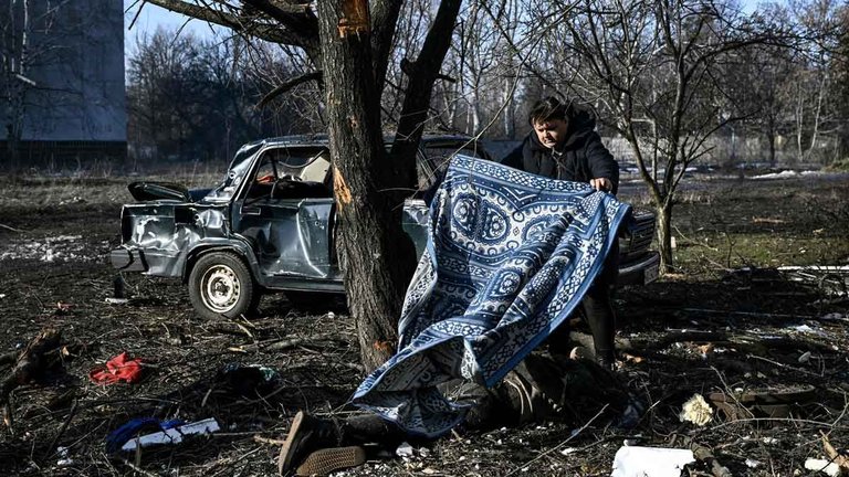 Rusia ataca Ucrania. En la foto, un hombre usa una alfombra para cubrir un cuerpo que descansa en el suelo, en la ciudad ucraniana de Chuguiv. /
AFP