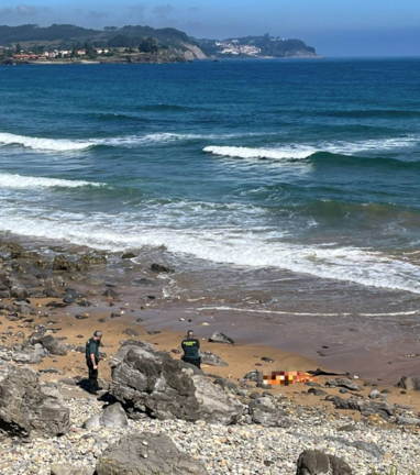 Agentes de la Guardia Civil ante el cuerpo sin vida del buceador aparecido en una playa de Caravia. / GUARDIA CIVIL
