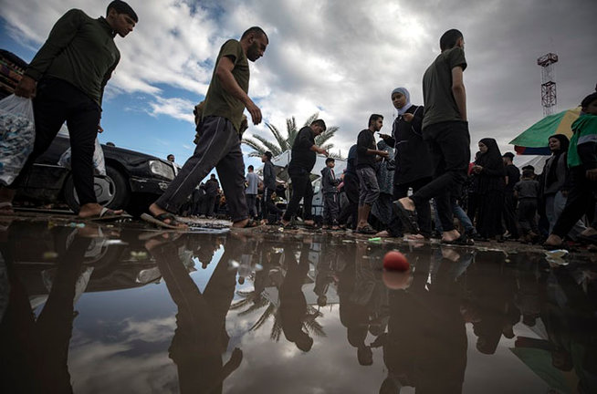Palestinos pasan junto a un charco de agua después de una noche lluviosa en un campamento temporal. EFE/HAITHAM IMAD