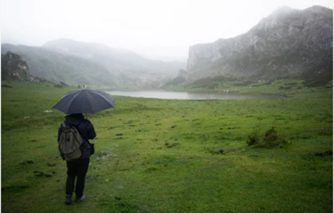 Una persona con un paraguas bajo la lluvia mirando un paisaje. / A.S.