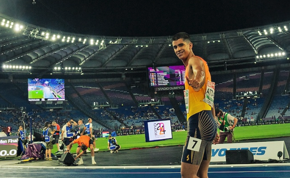 El atleta sonríe y saluda tras completar una carrera en el estadio, mostrando su satisfacción y optimismo durante la competición nocturna.