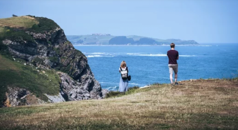 Dos personas de espaldas mirando al mar desde un acantilado en el Cantábrico.