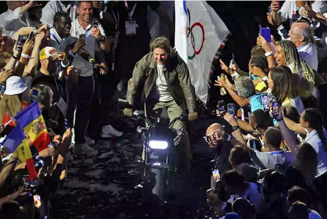 El actor estadounidense Tom Cruise, coge la bandera olímpica subido en una moto. / EP