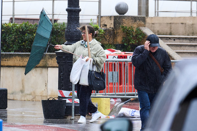 Varias personas tratan de cubrirse de la lluvia y el viento, en Santander. / EP